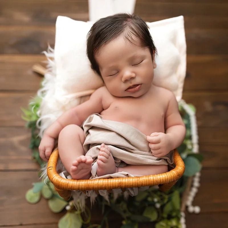 Ein schlafendes Baby ruht im kleinen Korbwagen auf einem weißen Kissen.
