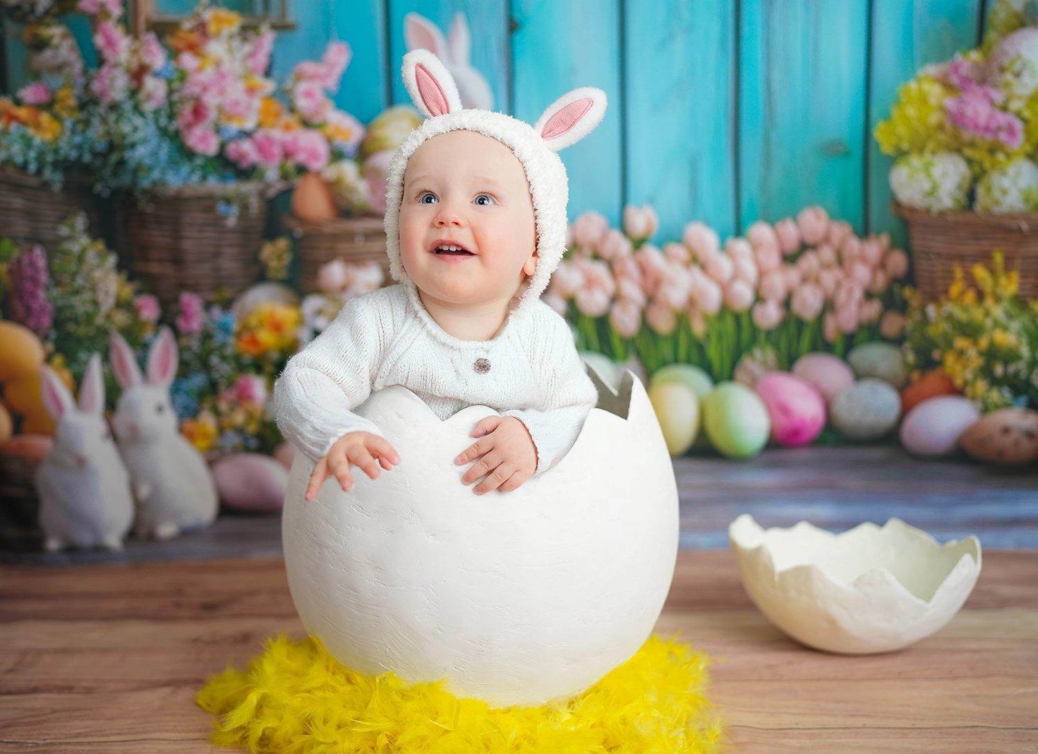 Ein Baby mit Hasenohren sitzt im weißen Dekoei vor bunten Blumen.