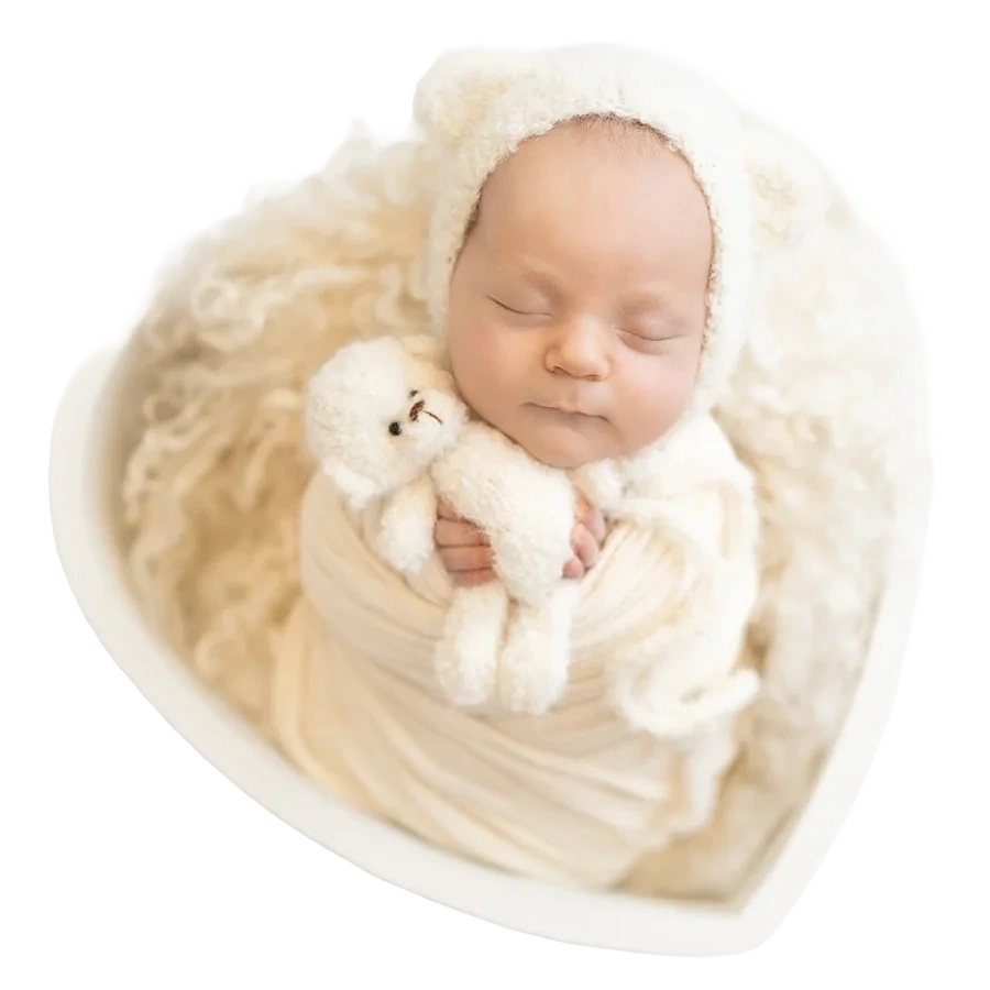 Ein schlafendes Neugeborenes hält einen kleinen Teddy im hellen Herzkörbchen.
