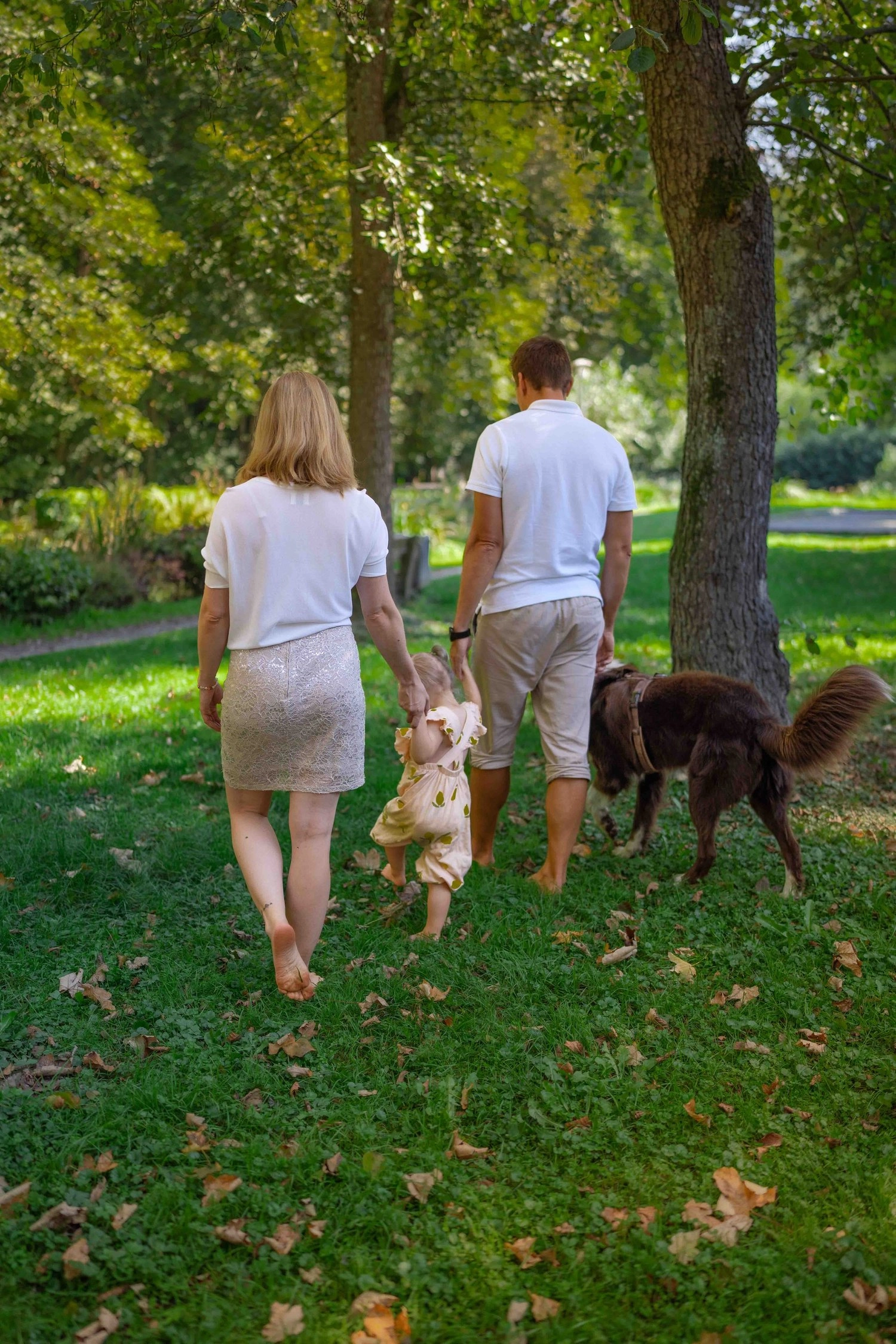 Ein Paar geht mit einem Hund durch einen grünen Park.