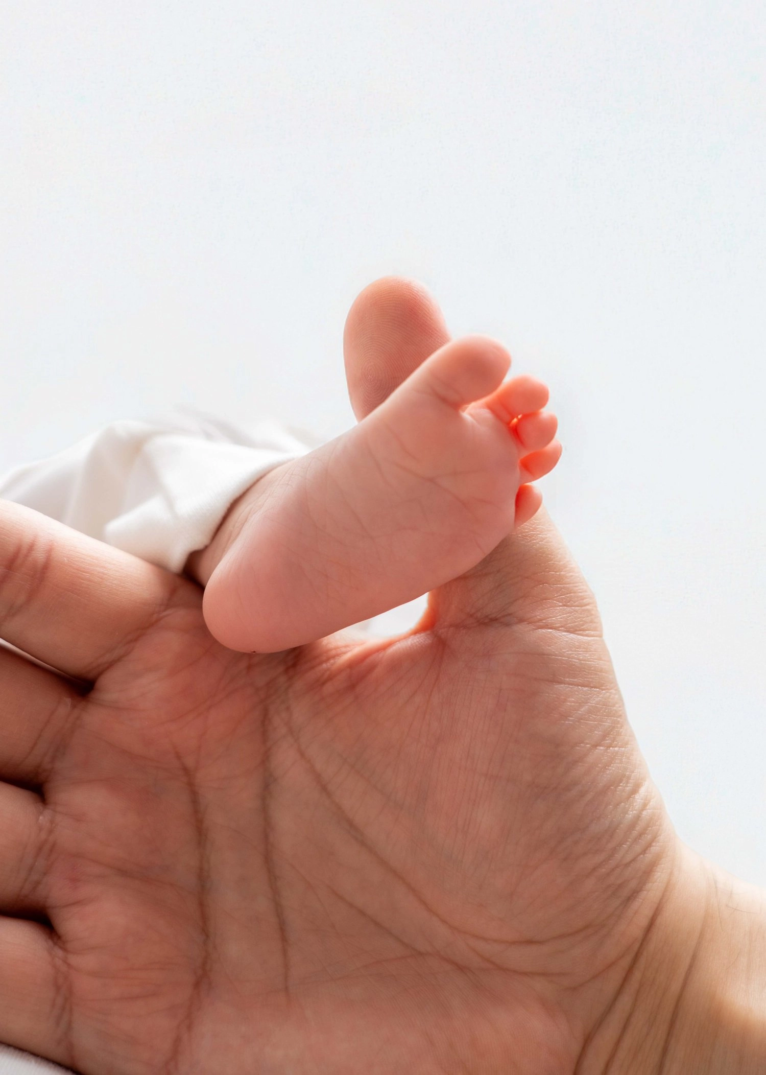Eine erwachsene Hand hält vorsichtig den kleinen Fuß eines Babys.