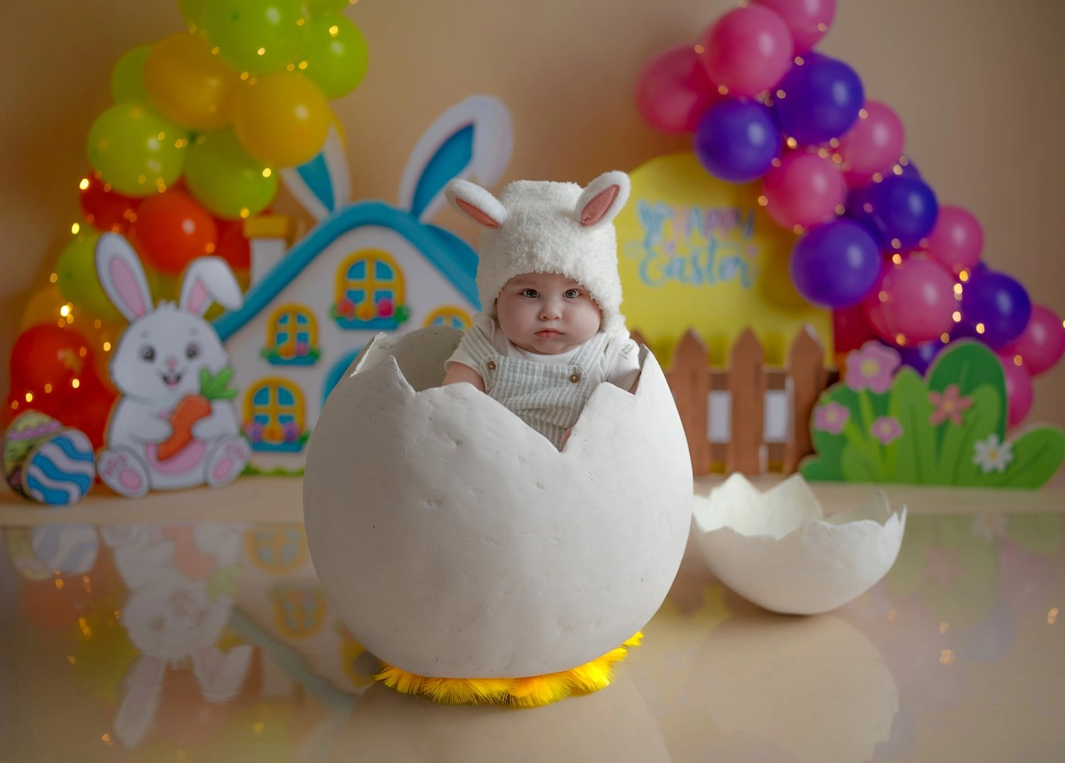 Ein Baby mit Hasenmütze sitzt im Dekoei vor einem bunten Häuschen.