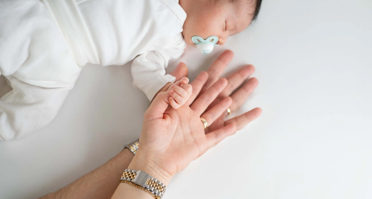 Die kleine Hand eines schlafenden Babys berührt eine erwachsene Hand.