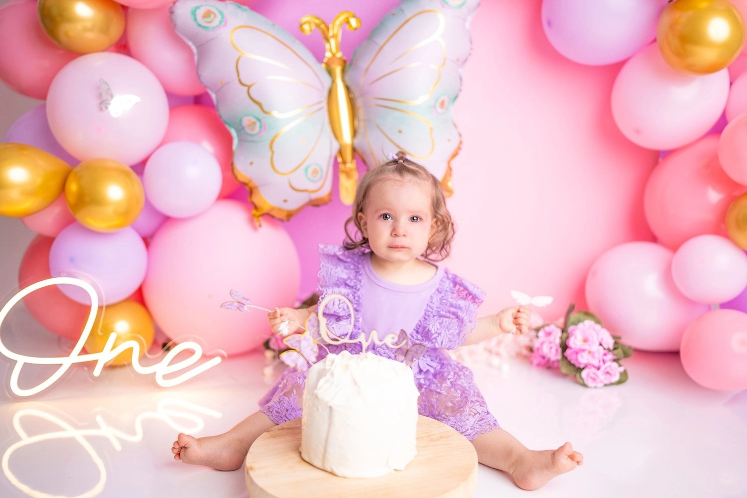 Ein Kind im lilafarbenen Kleid sitzt mit Torte vor einer Schmetterlingsdekoration.