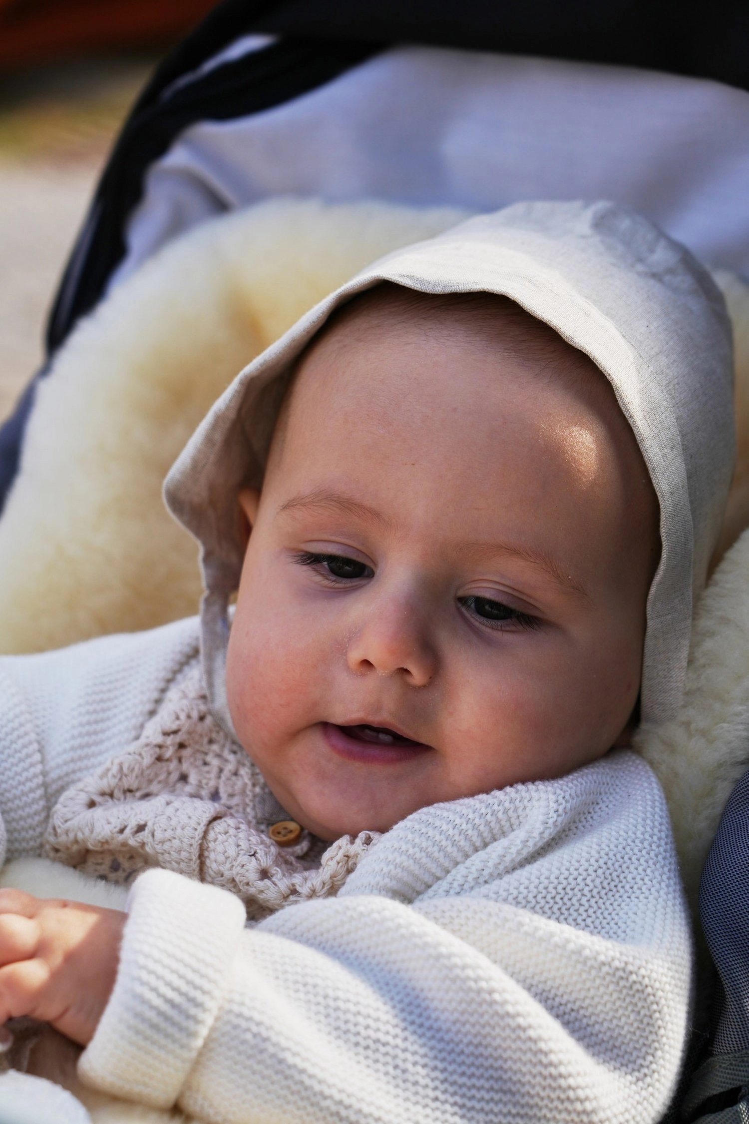 Ein Baby mit heller Haube lächelt aus seinem weich gepolsterten Kinderwagen.