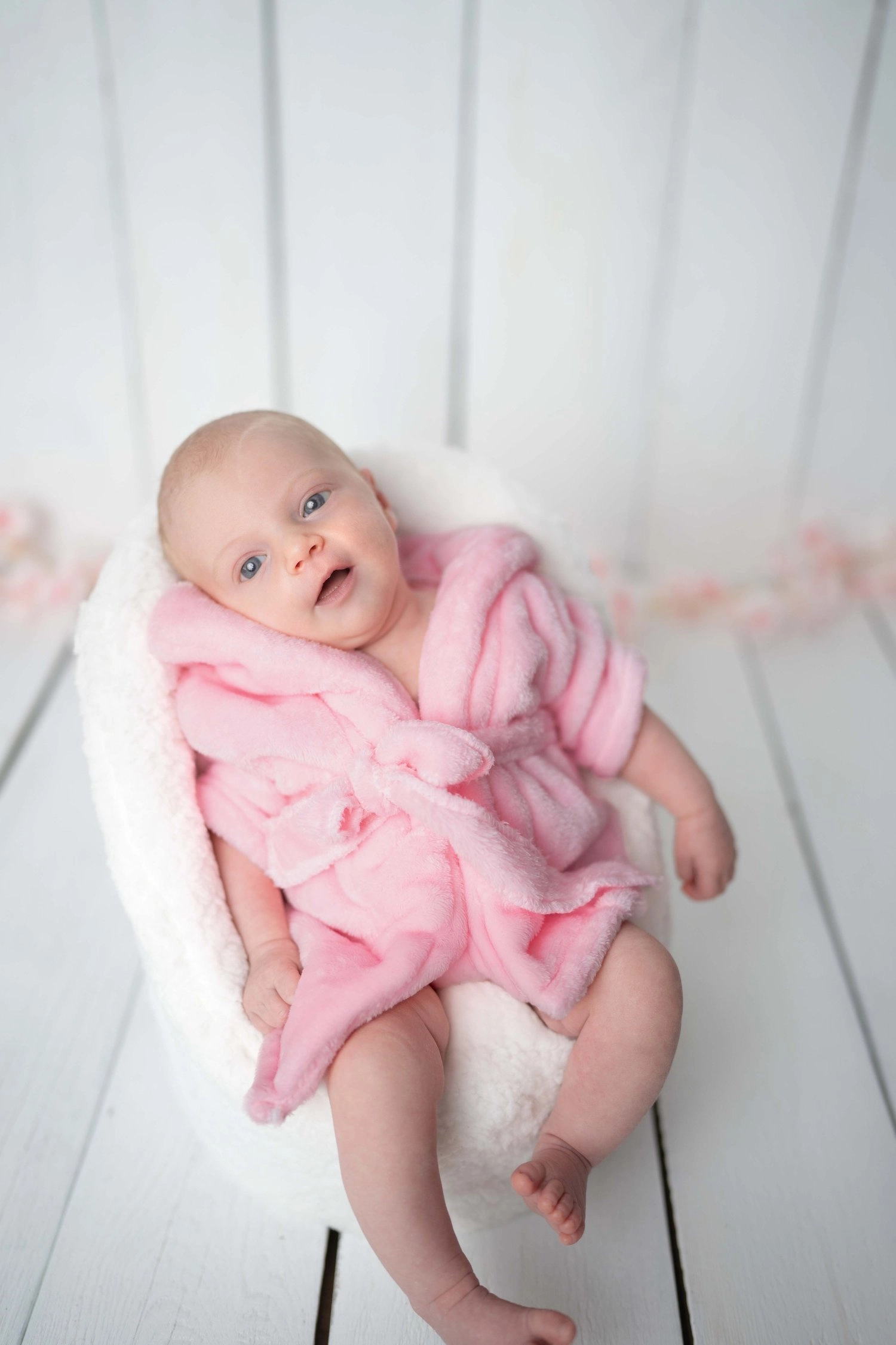 Ein Baby im rosa Bademantel liegt lächelnd auf einem kleinen Sessel.