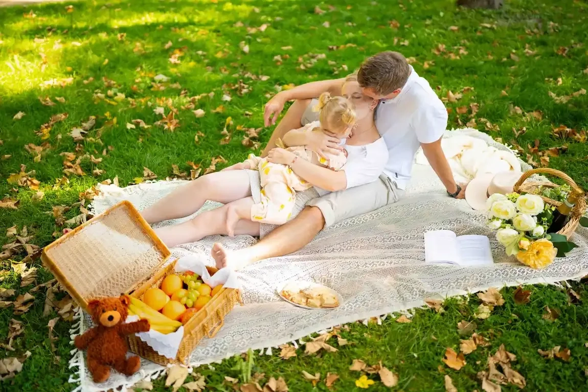 Zwei Erwachsene kuscheln mit einem Kind auf einer Picknickdecke im Grünen.