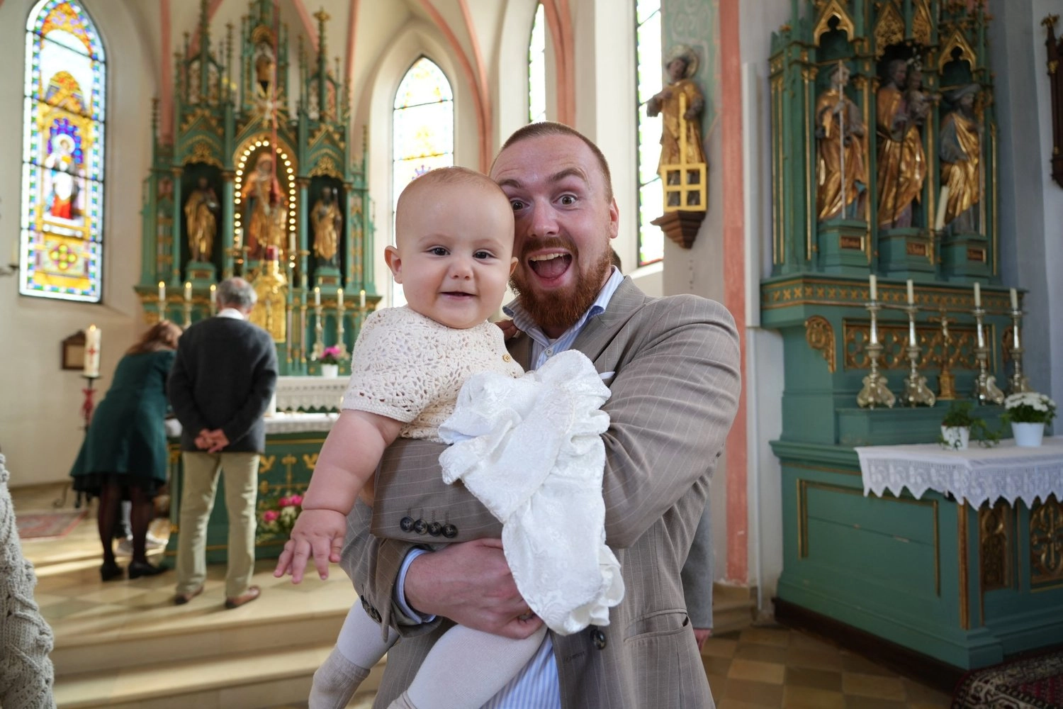 Ein Mann hält ein lachendes Baby vor einem goldenen Kirchenaltar.