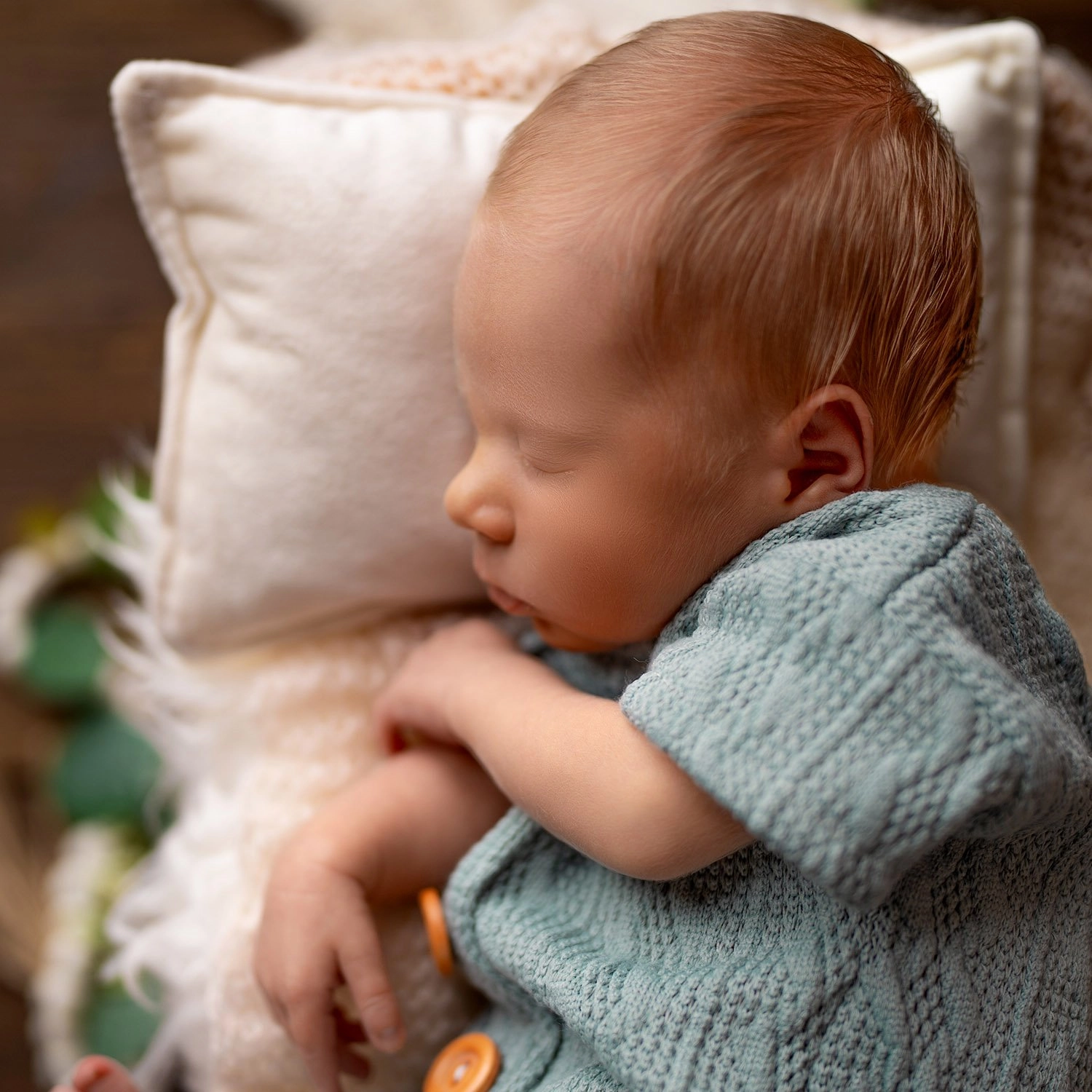 Ein schlafendes Baby ruht im blauen Strickoutfit auf einem Kissen.