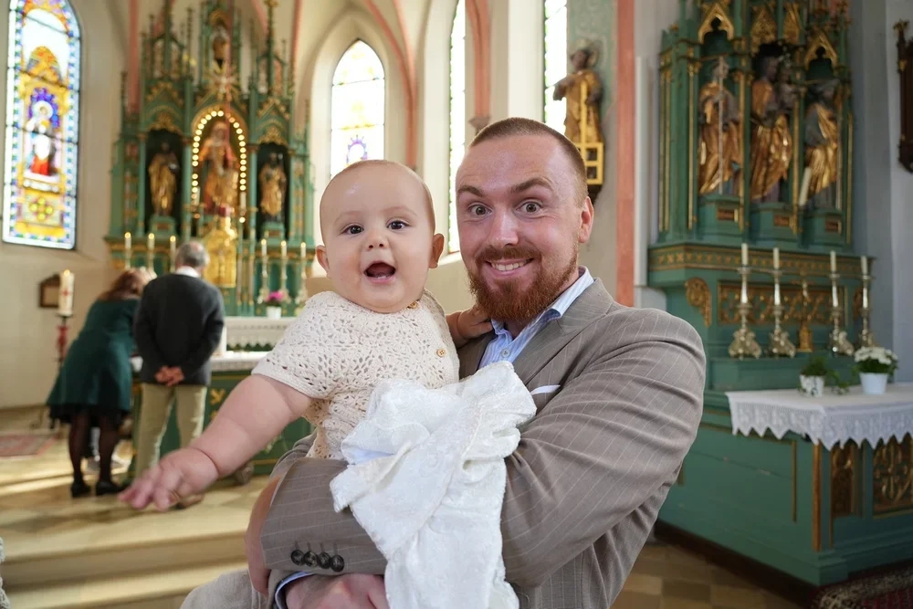 Ein Mann und ein Baby lächeln gemeinsam vor dem Kirchenaltar.
