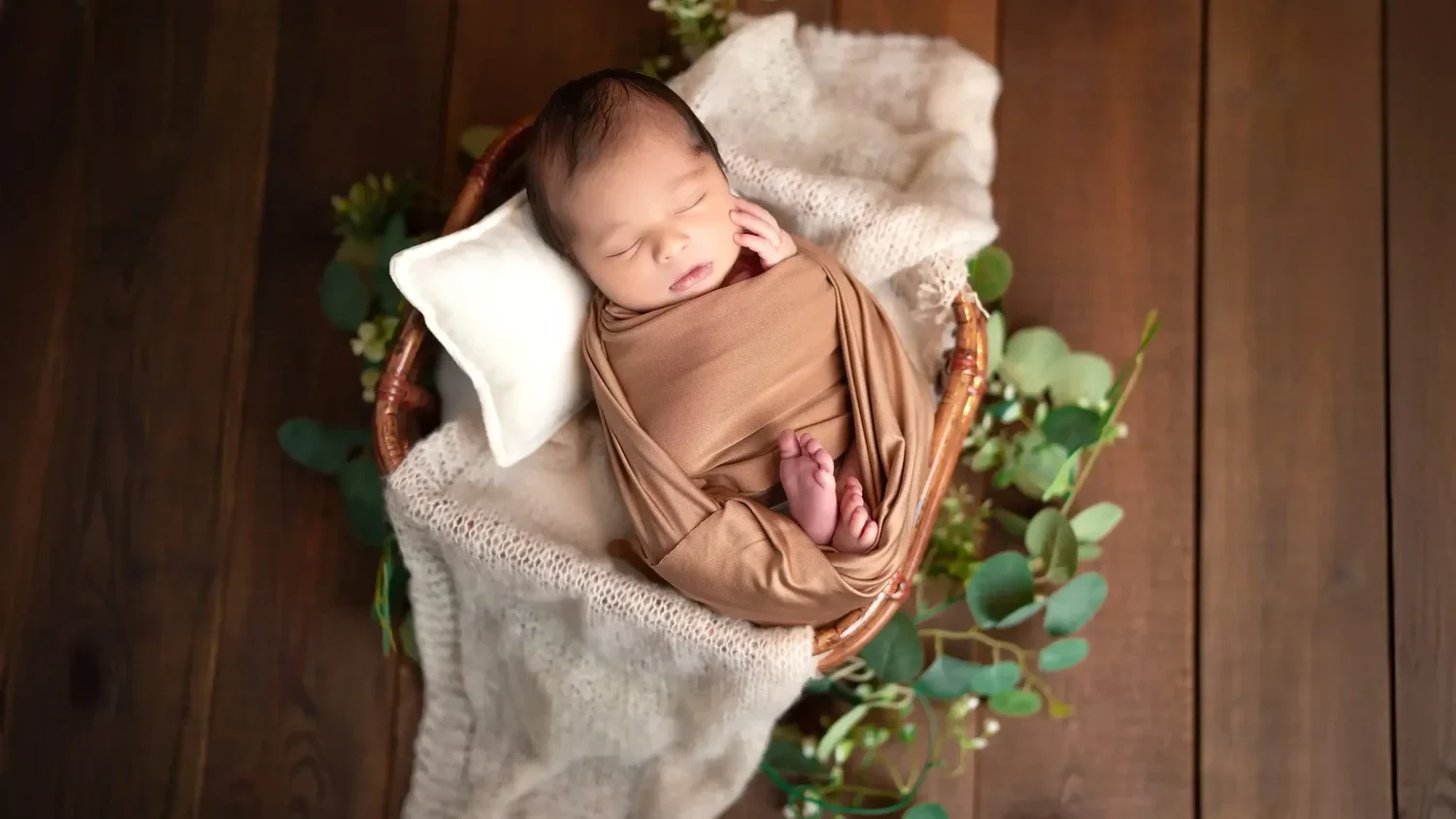 Ein schlafendes Baby liegt in braunem Stoff zwischen grünen Zweigen.