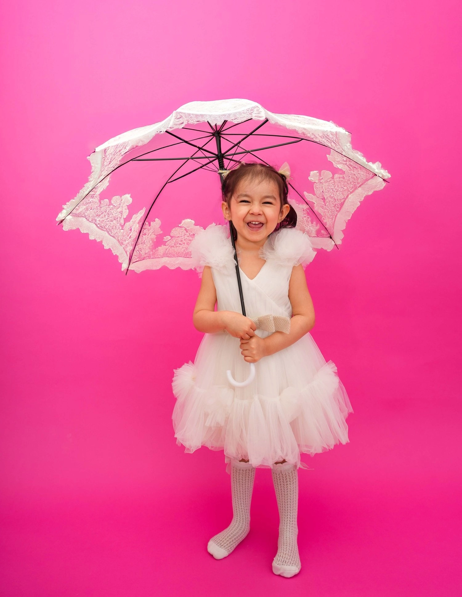 Ein Kind im weißen Kleid hält einen Spitzenschirm vor Pink.