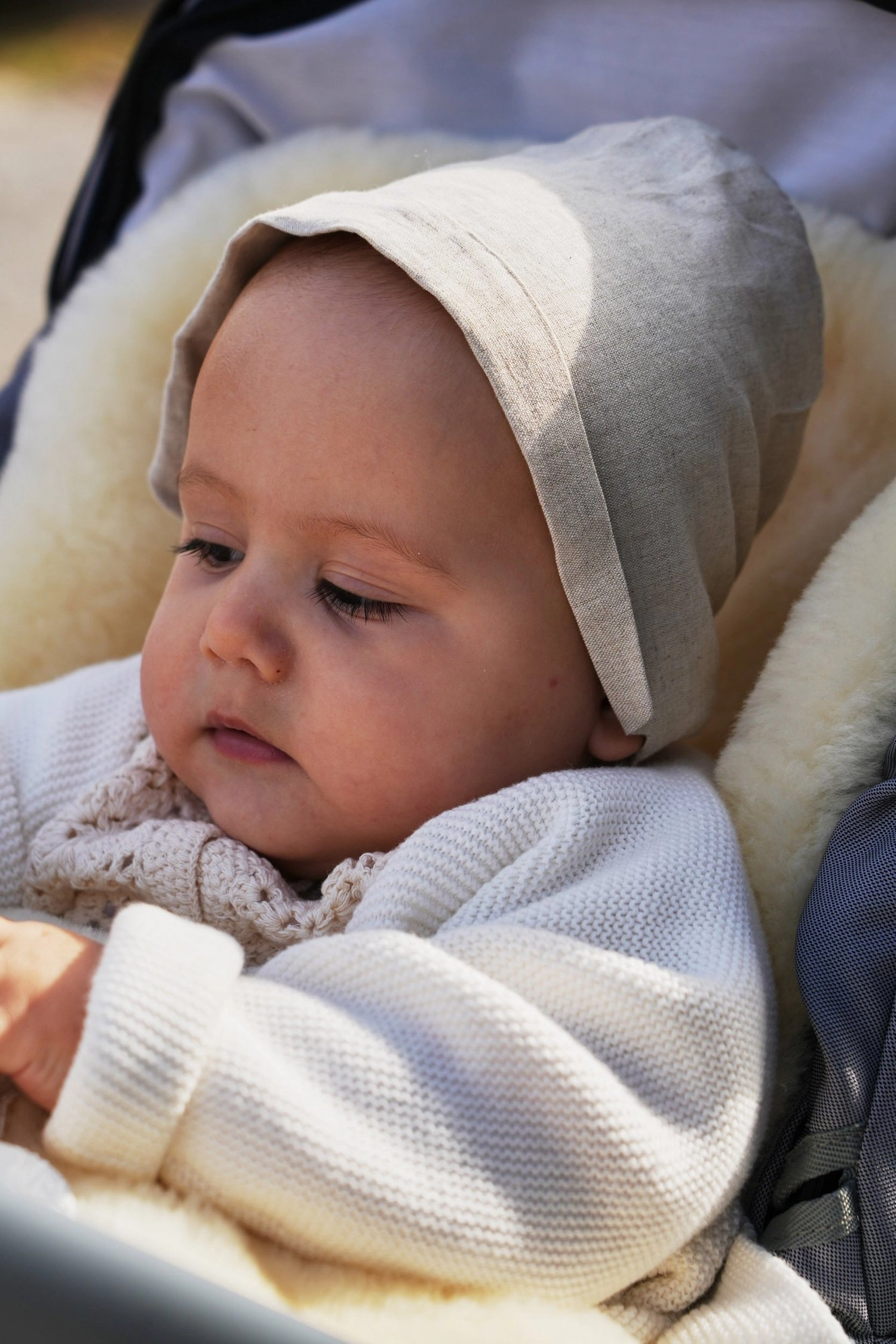 Ein Baby mit heller Strickhaube blickt aufmerksam aus dem Kinderwagen.