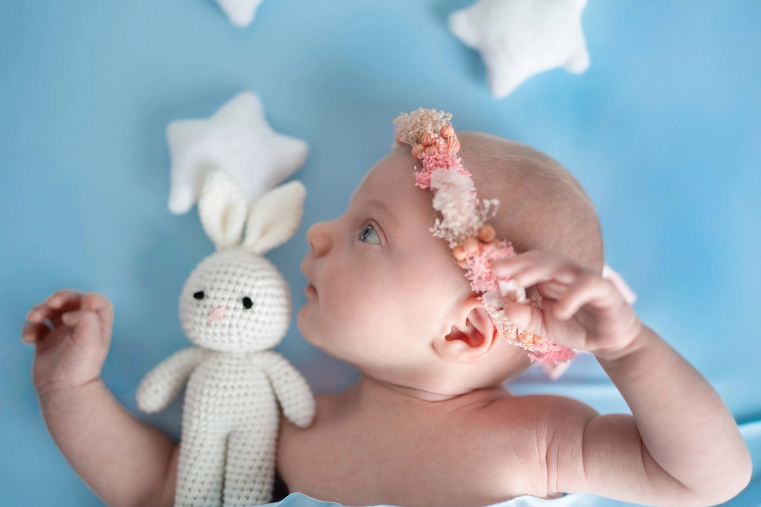 Ein Baby mit Blumenhaarband liegt neben einem weißen Häkelhasen.