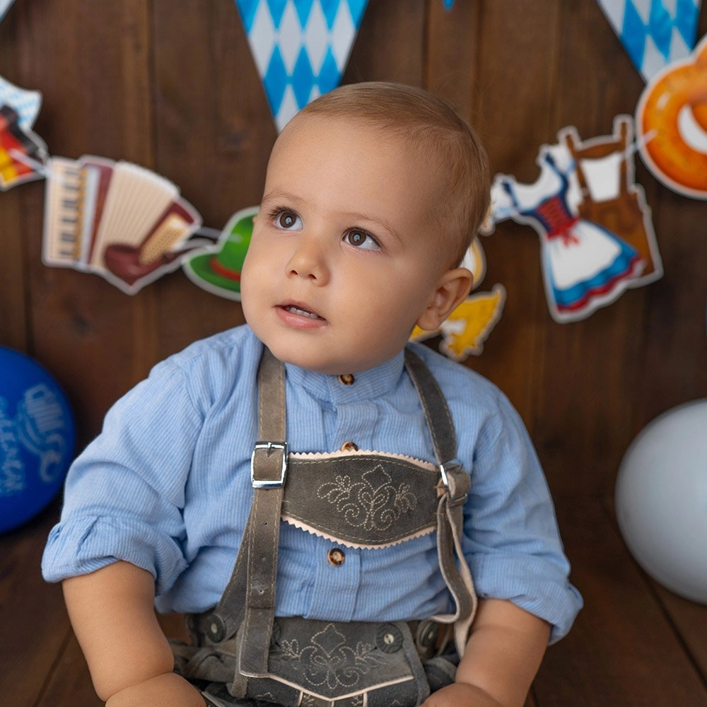 Ein Baby in blauer Tracht blickt vor einer Festkulisse zur Seite.