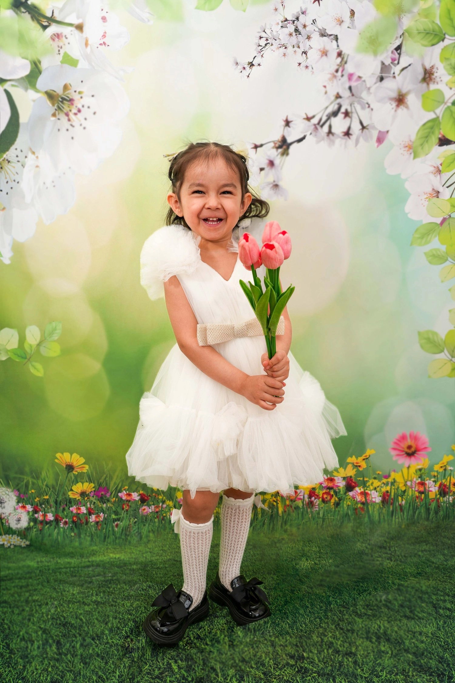 Ein Kind im weißen Kleid hält lachend einen Strauß Tulpen.