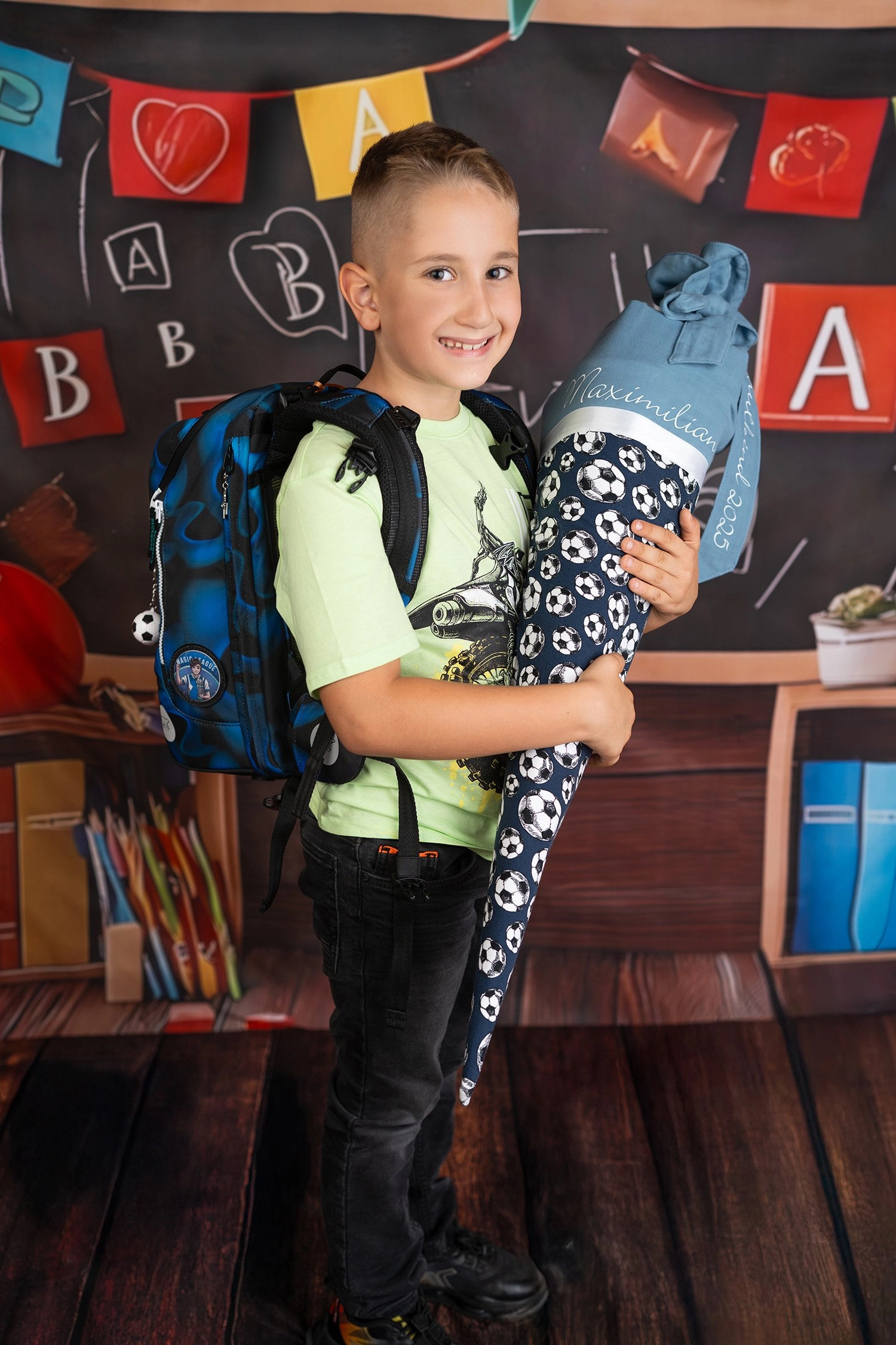 Ein Schulkind mit blauer Schultüte steht vor einer Tafel und Bücherregalen.