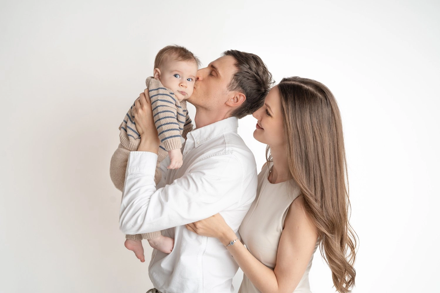Ein Mann küsst das gehaltene Baby, während eine Frau lächelnd zusieht.