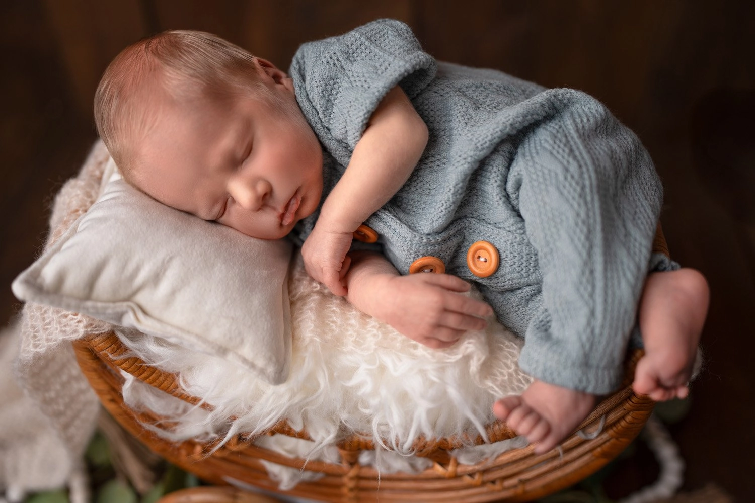 Ein schlafendes Baby liegt seitlich im Körbchen mit blauem Strickoutfit.