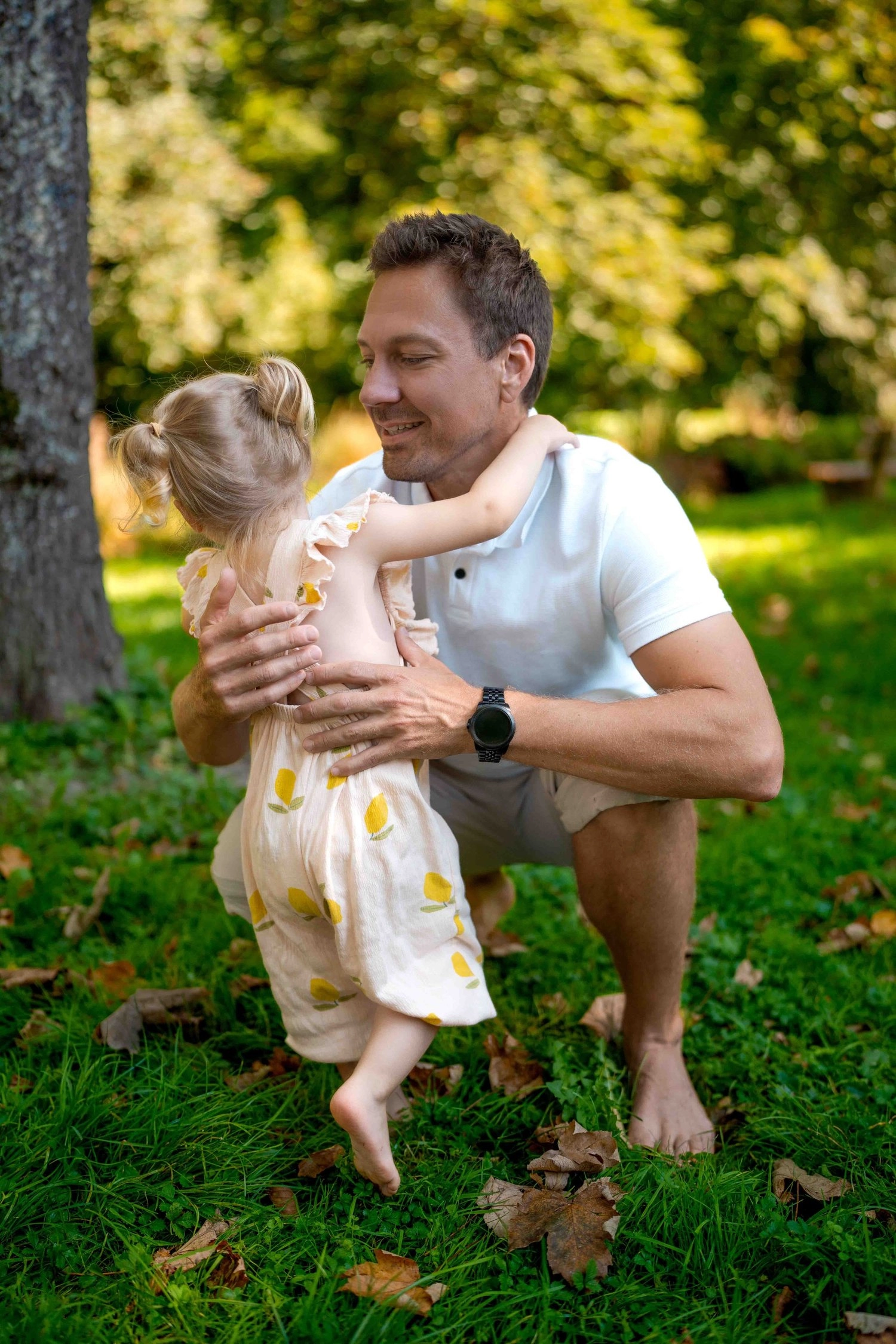 Ein Mann kniet im Park und hält ein kleines Kind.