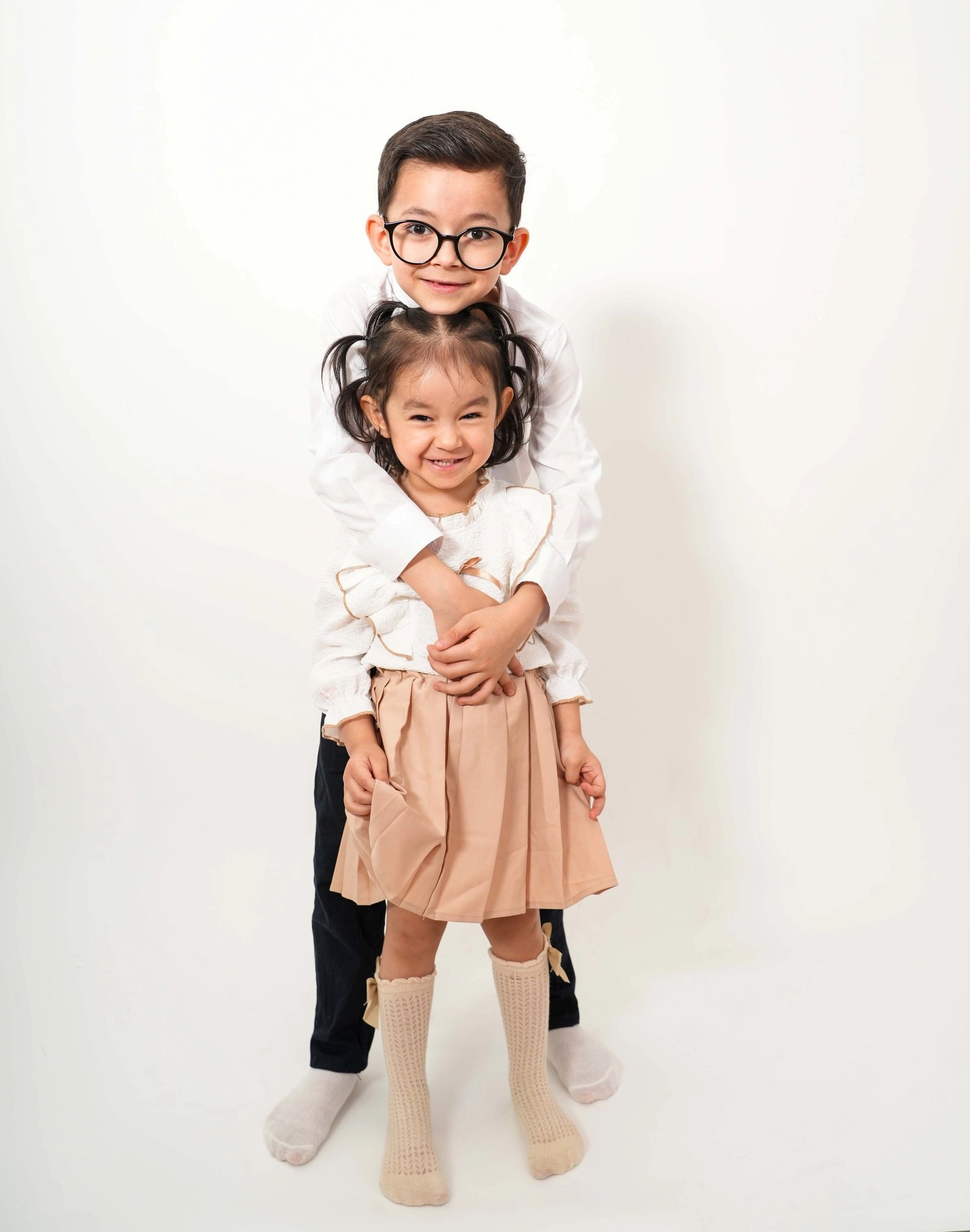 Ein Kind mit Brille umarmt ein kleineres Kind von hinten.