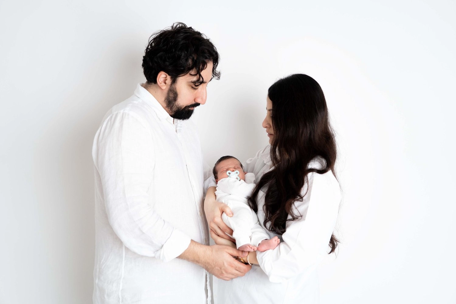 Ein Paar in weißer Kleidung hält gemeinsam den runden Babybauch.