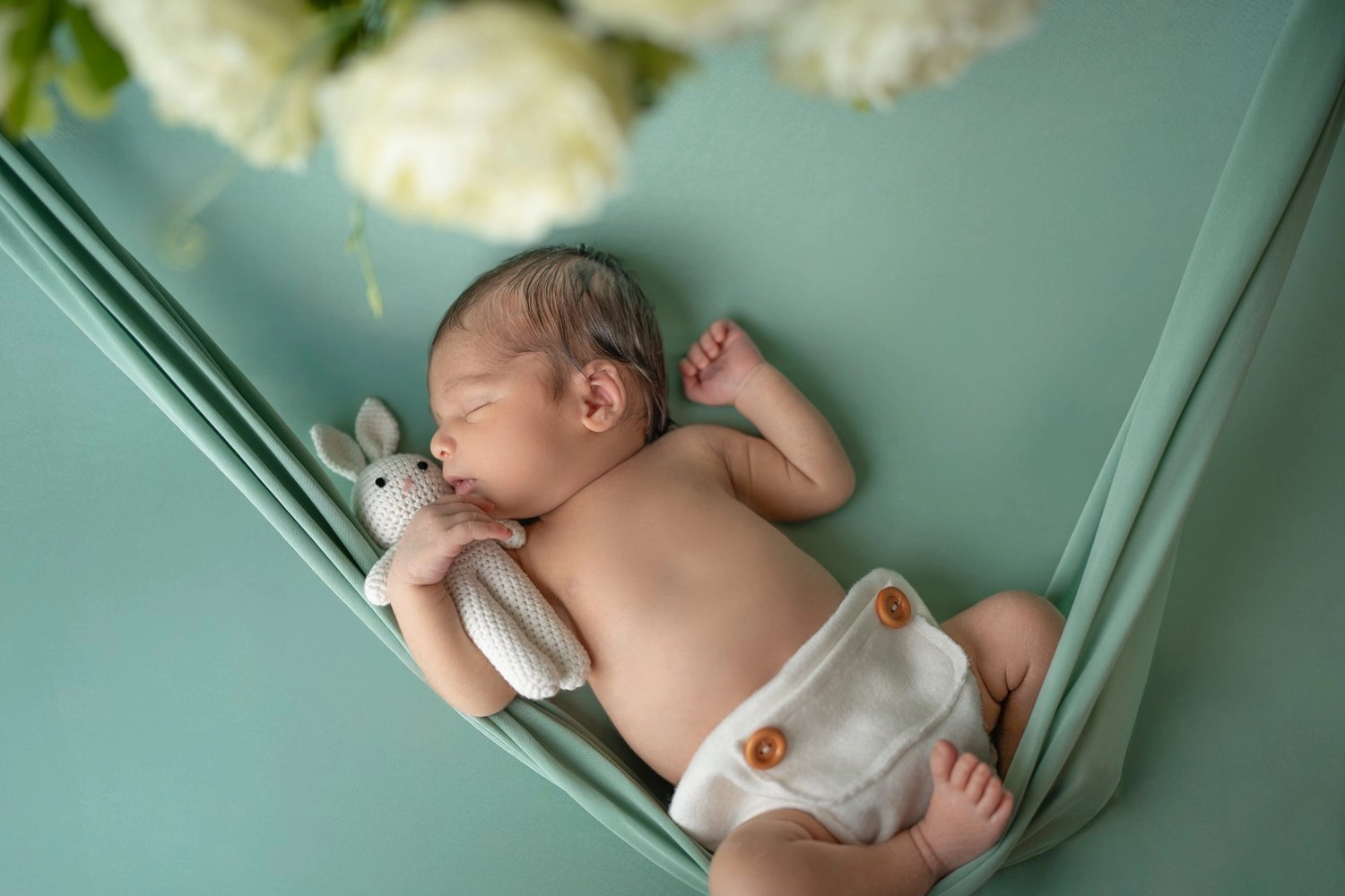 Ein schlafendes Baby liegt mit Kuscheltier in einer grünen Stoffhängematte.