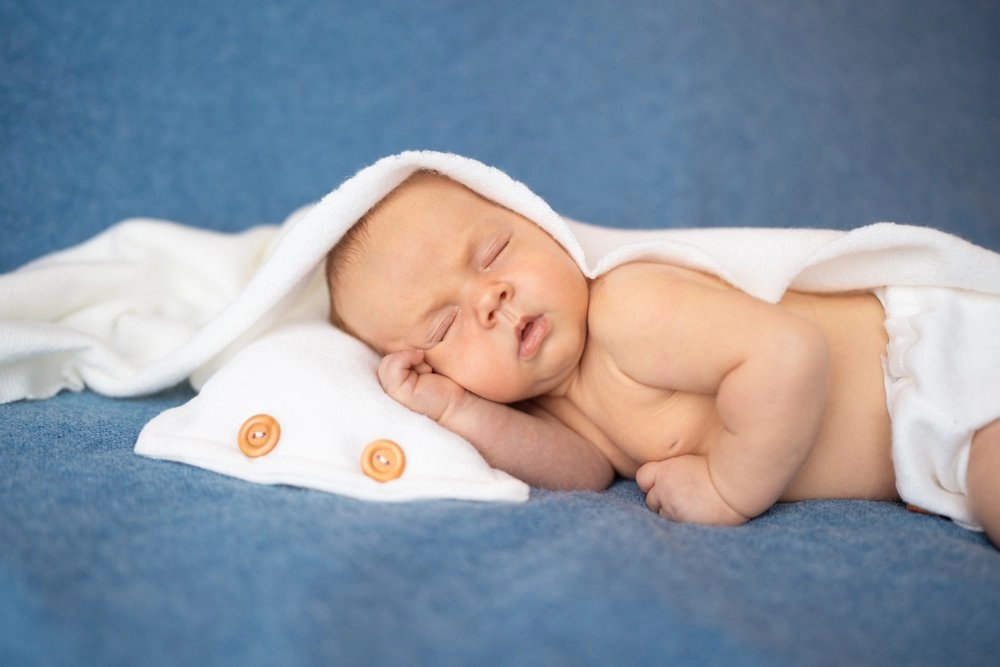 Ein schlafendes Baby liegt auf Blau unter einer weichen weißen Decke.