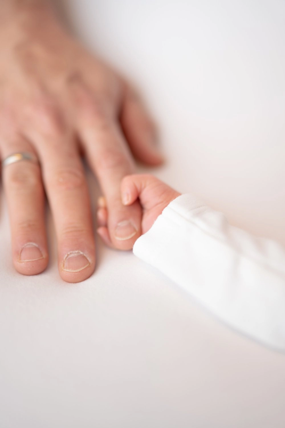 Eine erwachsene Hand liegt behutsam über der kleinen Hand eines Babys.