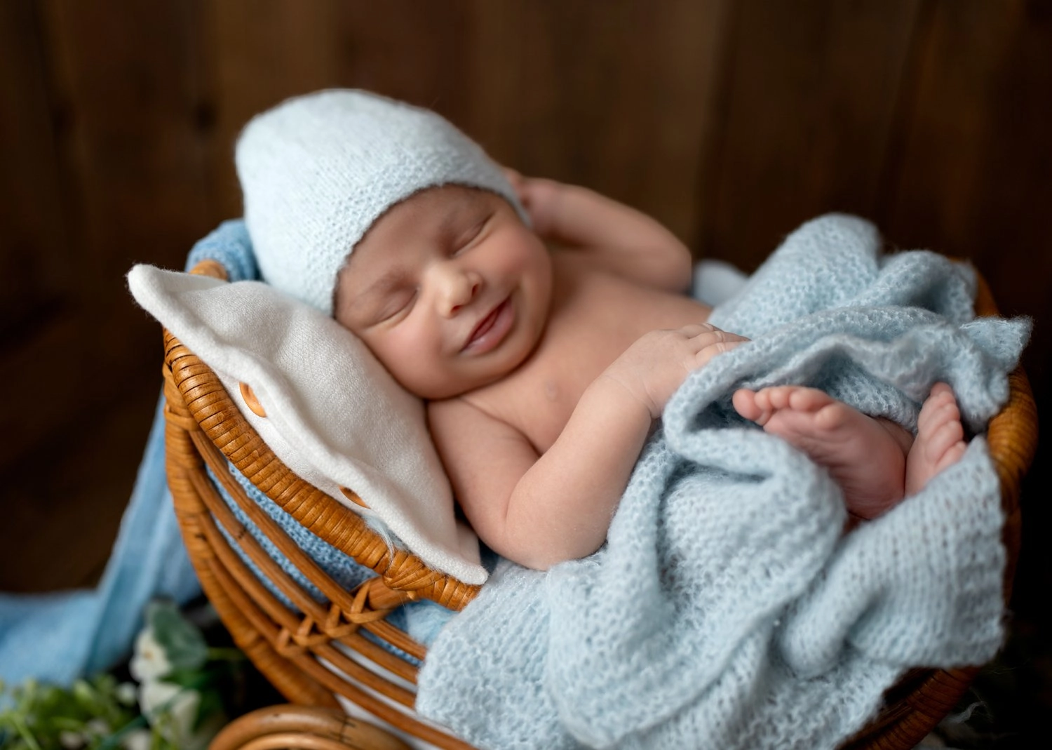 Ein schlafendes Baby mit blauer Mütze liegt lächelnd im Korbwagen.