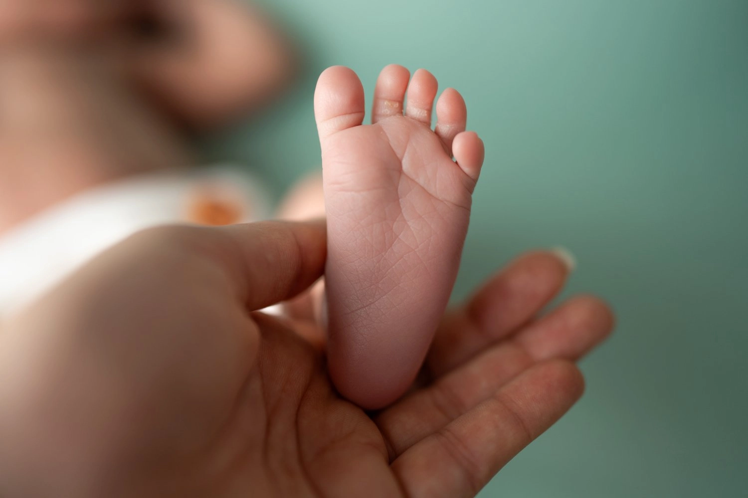Eine erwachsene Hand hält den kleinen Fuß eines liegenden Babys.