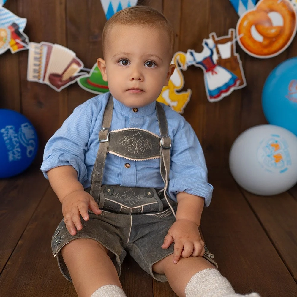 Ein Baby in blauer Tracht sitzt vor einer bunten Festgirlande.