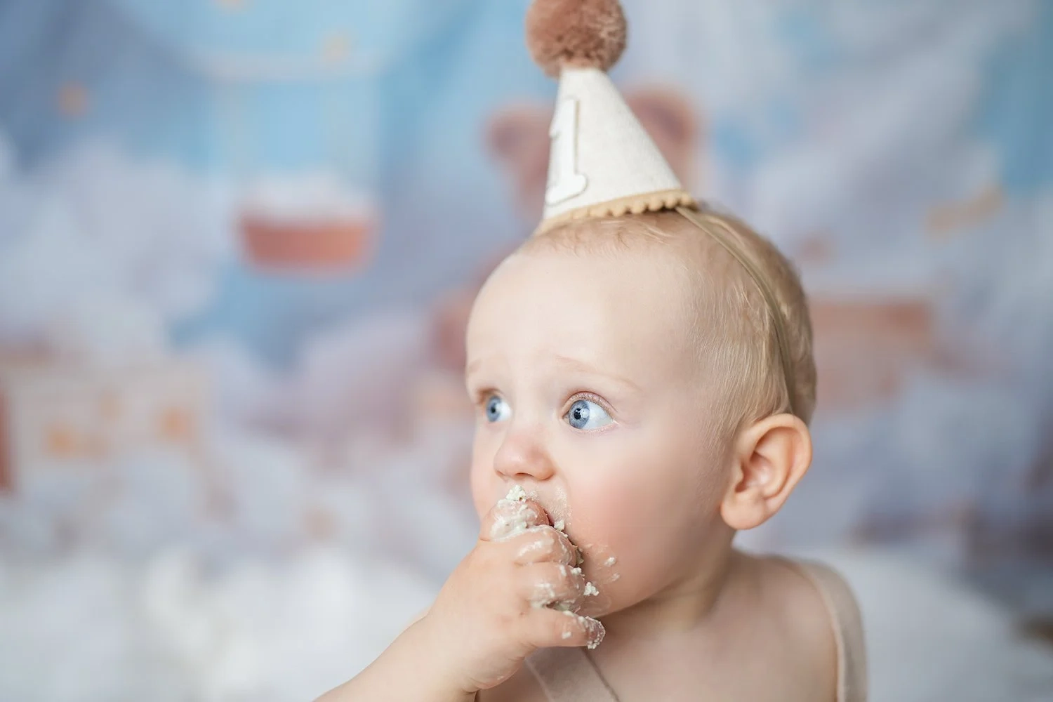 Ein Baby mit Geburtstagshut probiert Tortencreme von seinen kleinen Fingern.