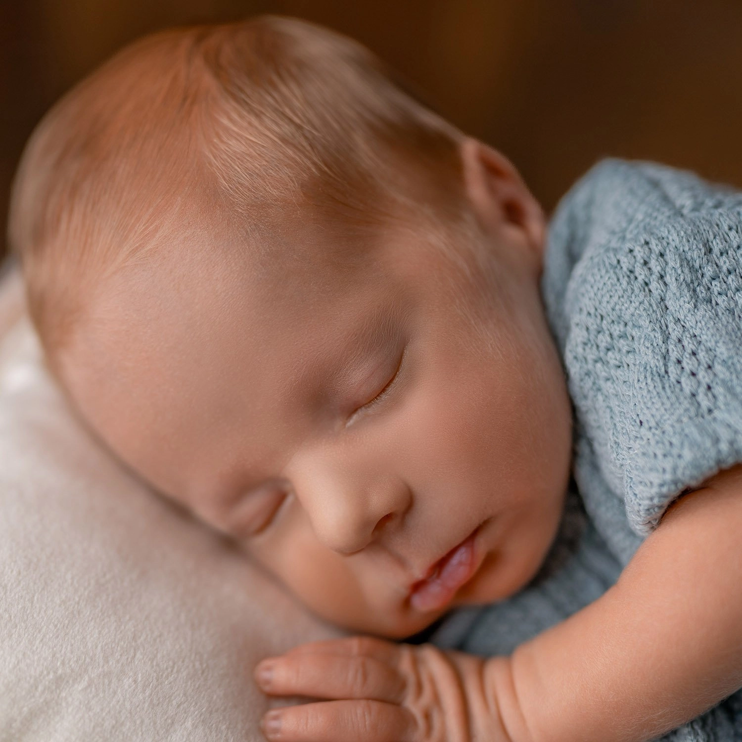 Ein schlafendes Baby im blauen Strickoutfit legt die Hand neben sein Gesicht.