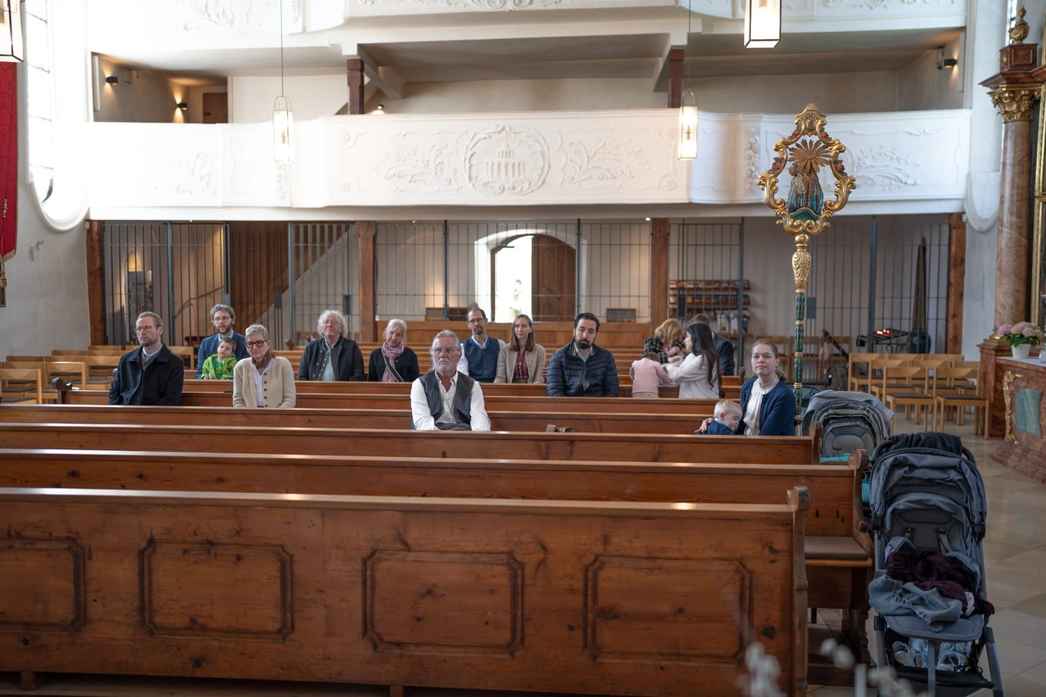 Gäste sitzen verteilt in hölzernen Kirchenbänken während einer Feier.