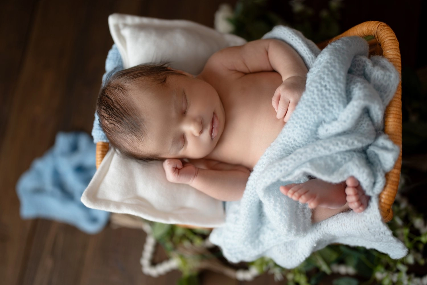 Ein schlafendes Baby kuschelt sich im Körbchen unter ein blaues Tuch.