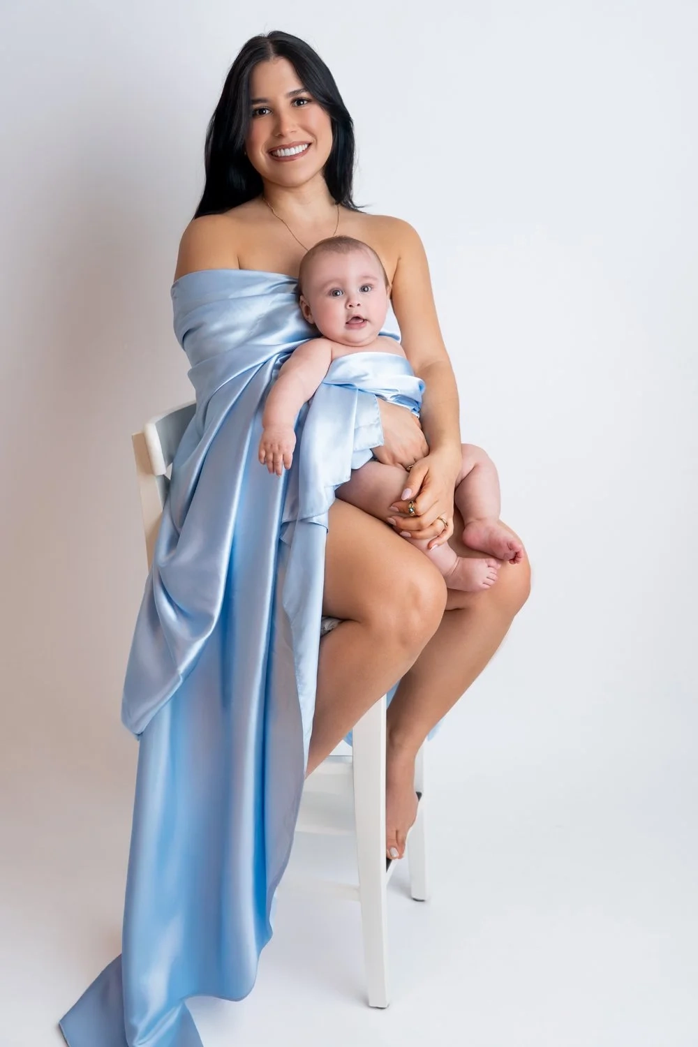 Eine lächelnde Frau hält ein Baby, während blauer Stoff herabfällt.