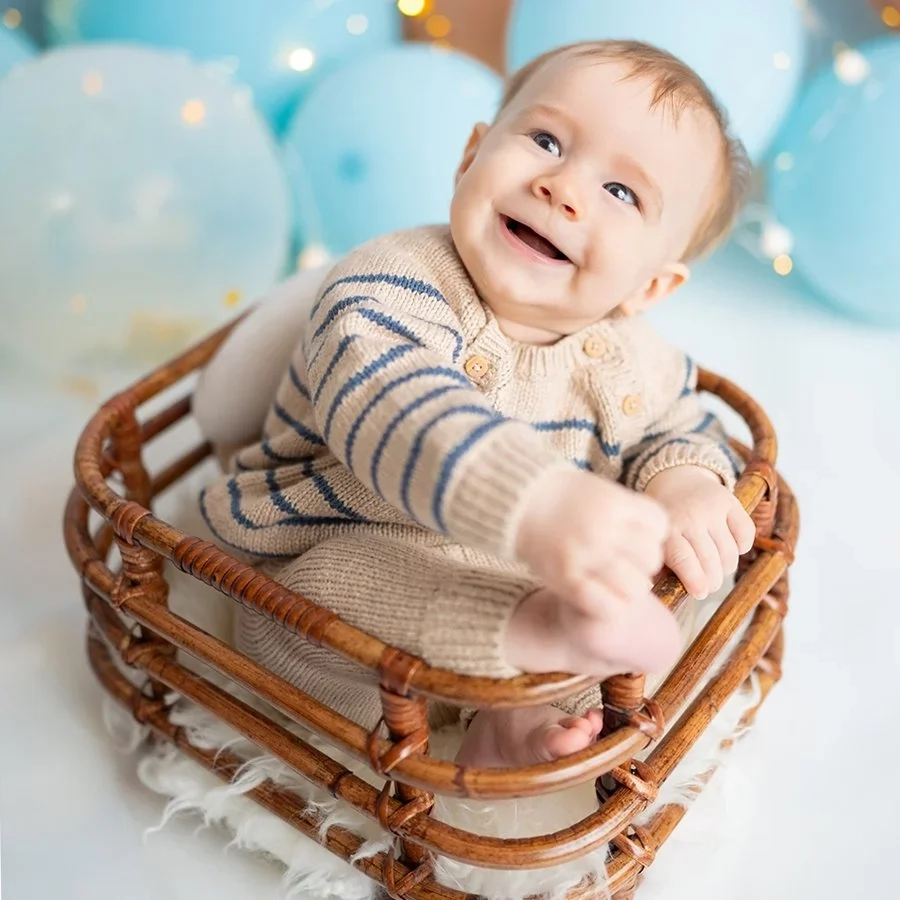 Ein lachendes Baby im Streifenpullover sitzt in einem kleinen Korb.