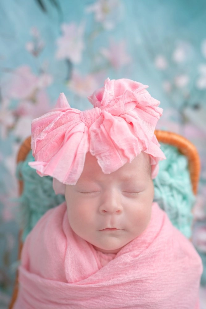 Ein schlafendes Baby trägt eine große rosa Schleife und rosa Tuch.