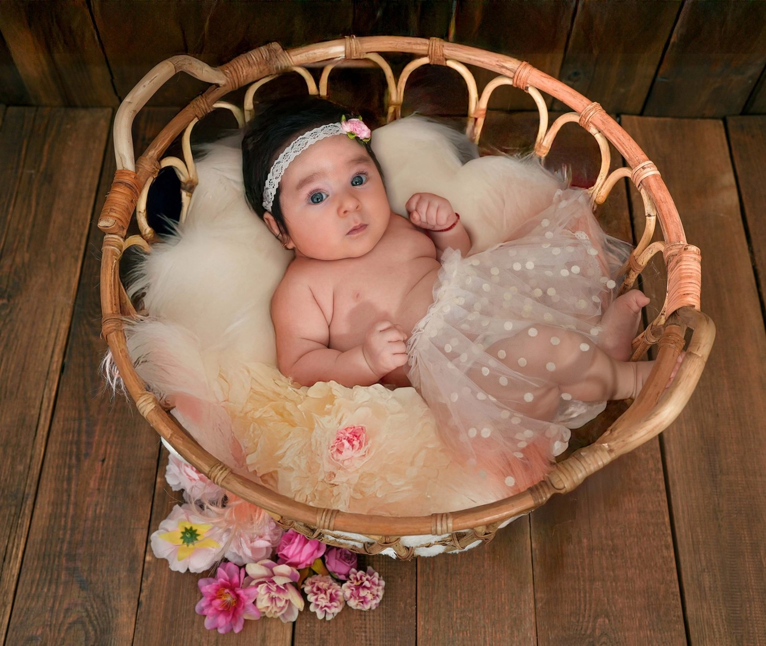 Ein waches Baby liegt im runden Korb neben zarten Blüten.