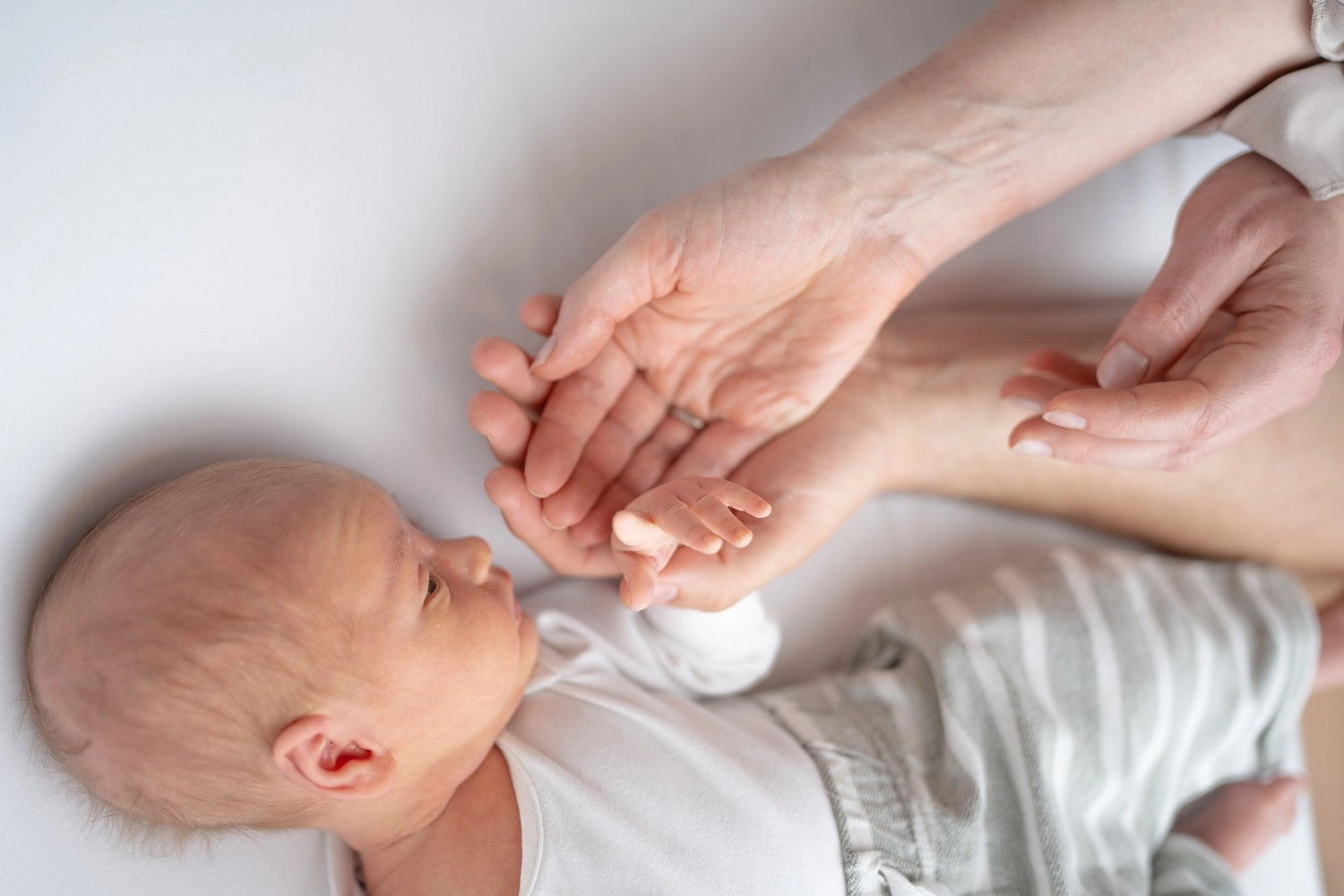 Ein liegendes Baby greift mit kleinen Fingern nach erwachsenen Händen.