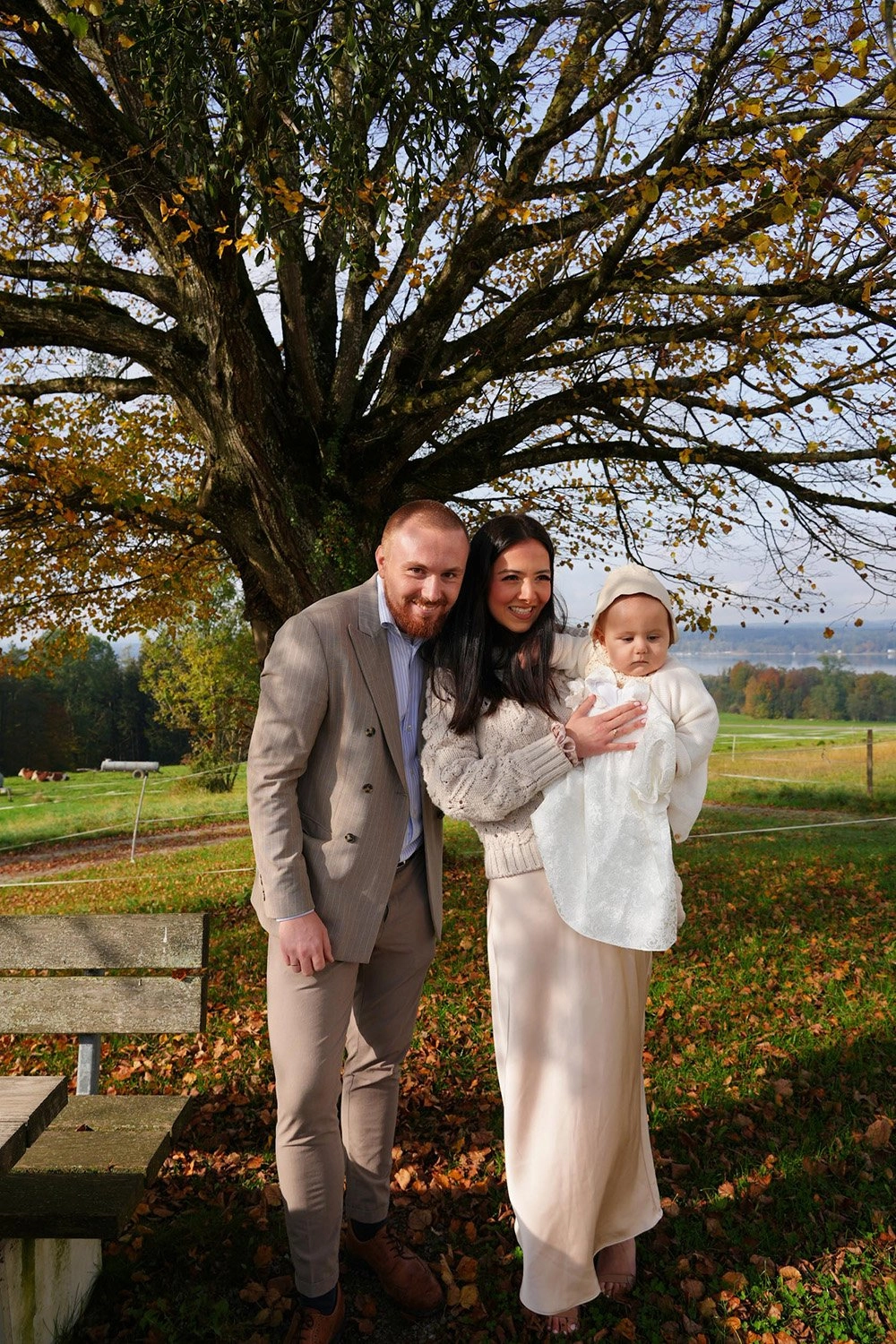 Zwei Erwachsene halten ein Baby und stehen unter einem großen Baum.