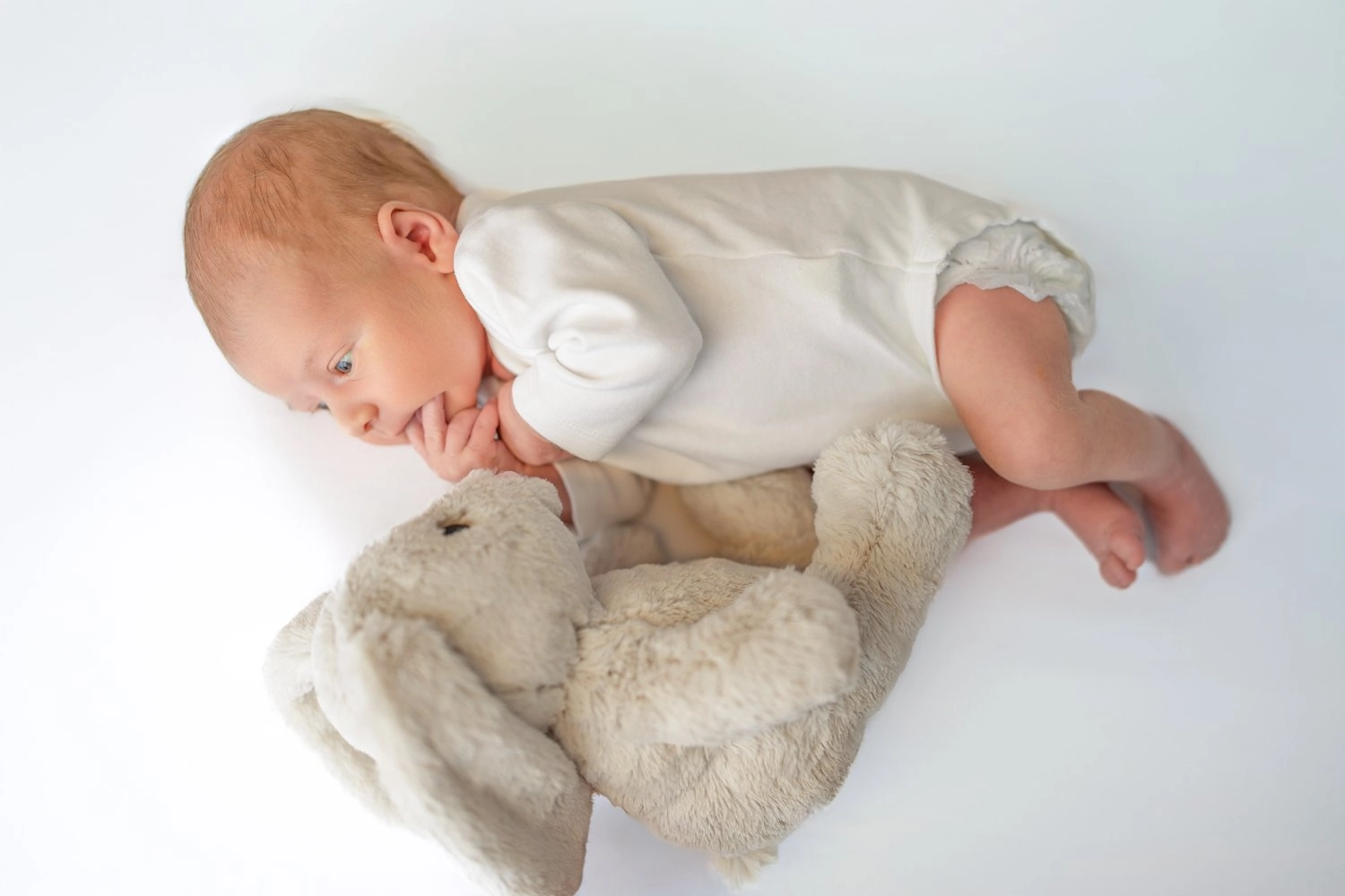 Ein schlafendes Baby in weißer Kleidung kuschelt mit einem hellen Stoffhasen.