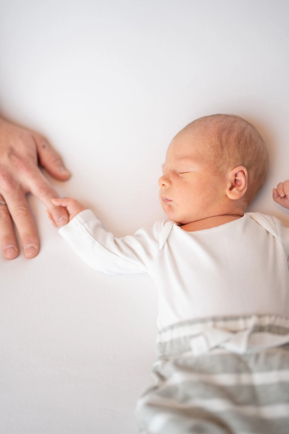 Ein liegendes Neugeborenes berührt mit seiner Hand eine erwachsene Hand.