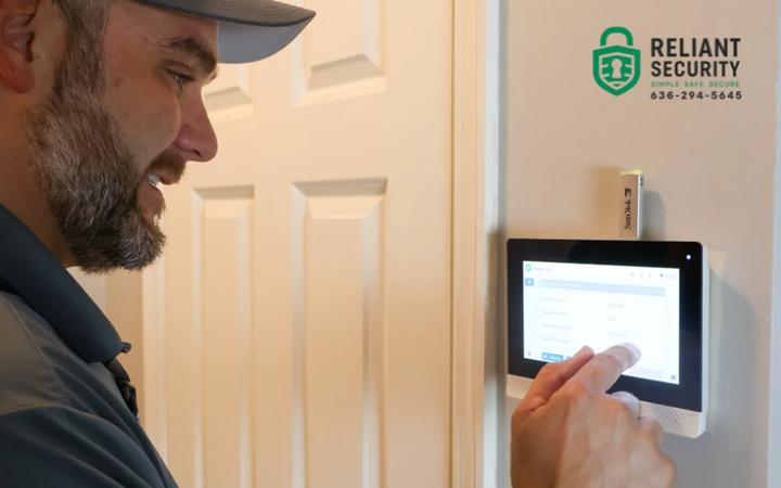A Reliant Security technician operating a wall-mounted alarm touchscreen panel inside a home.