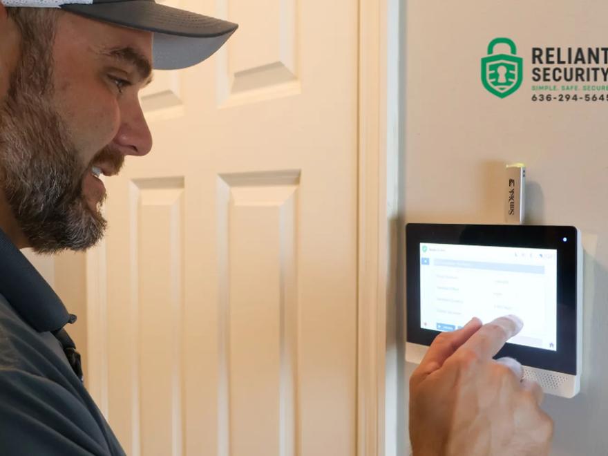 A Reliant Security technician operating a wall-mounted alarm touchscreen panel inside a home.
