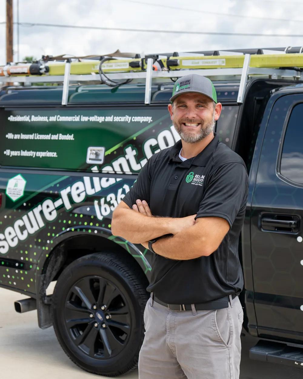 A Reliant Security technician standing in front of a branded Reliant service truck.