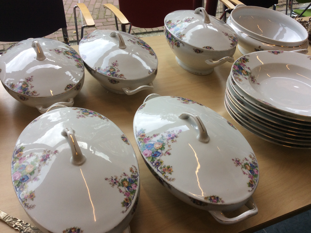 White porcelain soup tureens and soup plates with a flower pattern on a wooden table