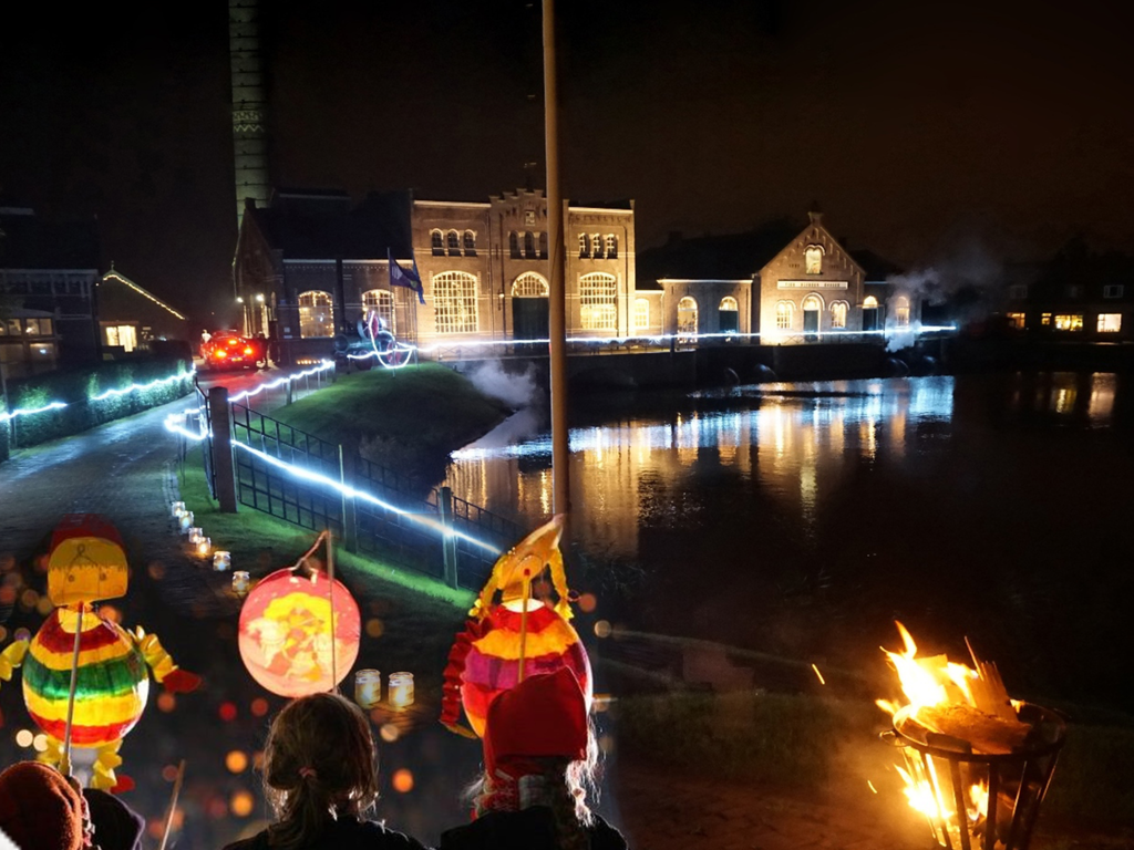 Het verlichte stoomgemaal aan het water in de avond, met lampionnen en een vuurkorf op de voorgrond