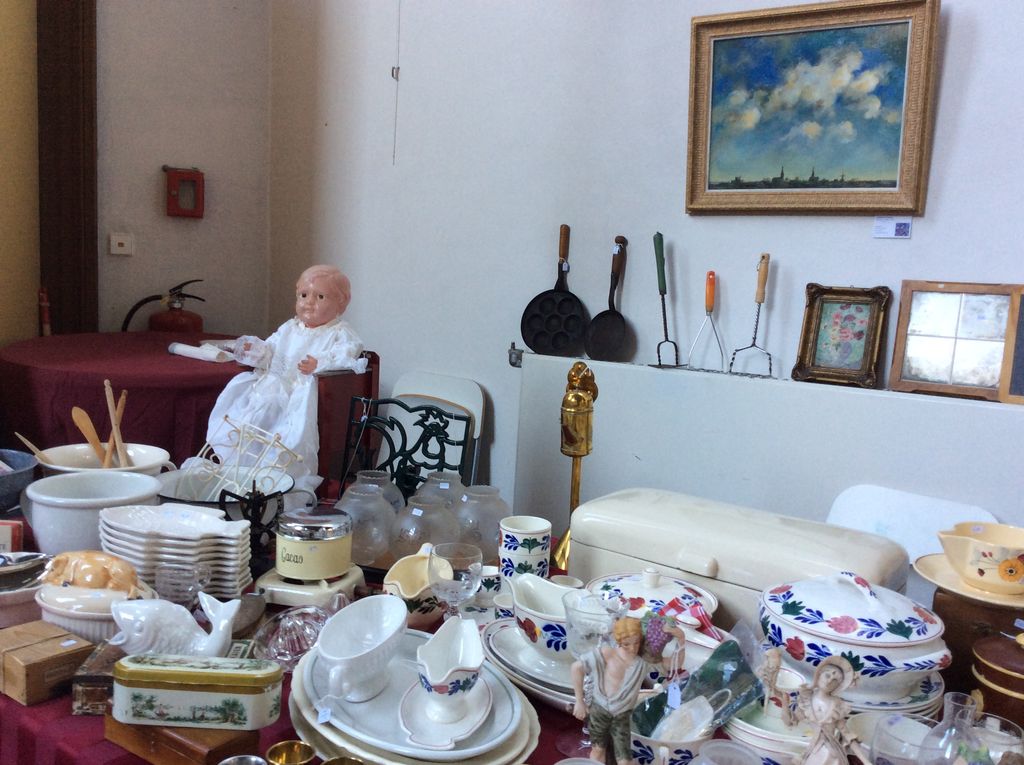 Kraam met een oude pop in doopjurk, Boerenbont-servies, broodtrommel, pannetjes en een schilderij aan de muur